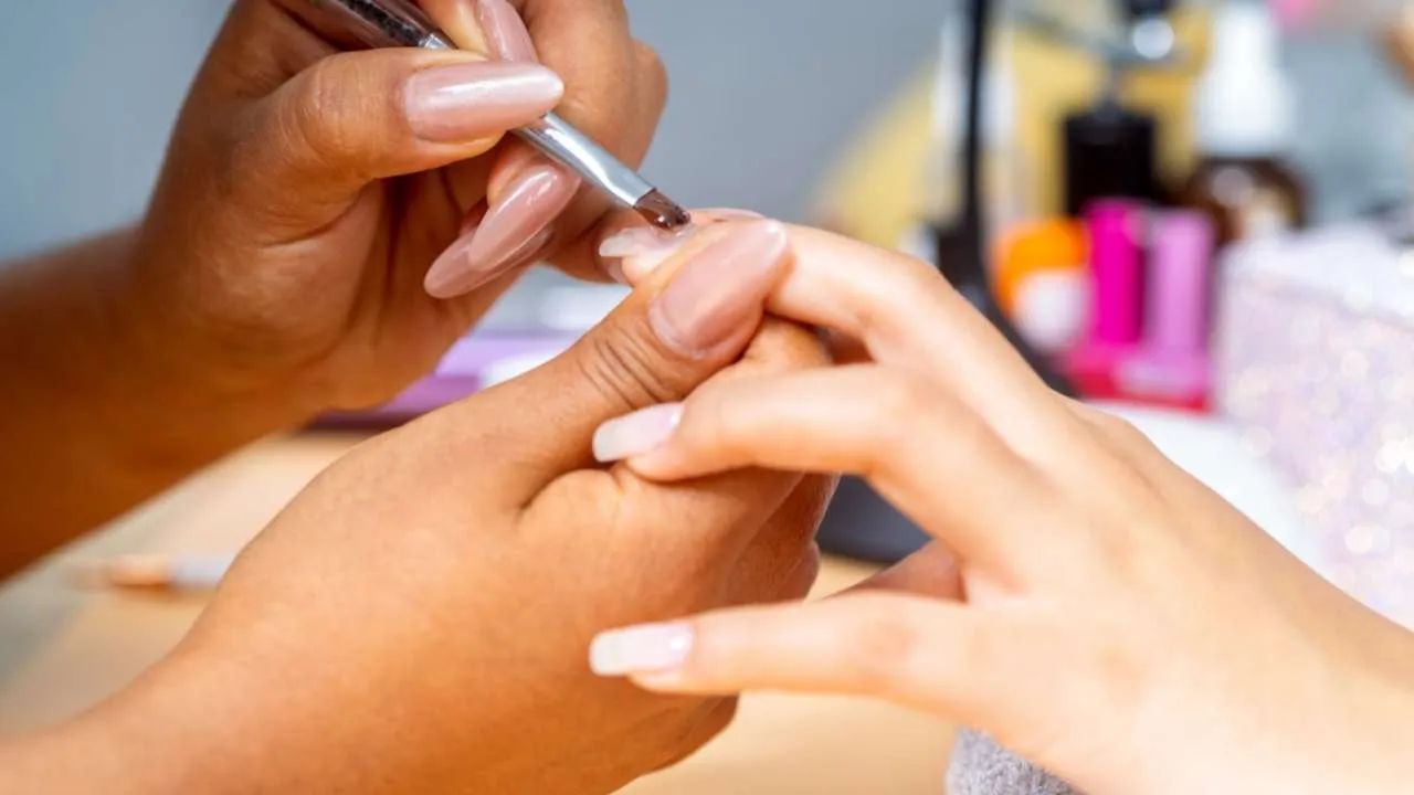 Nail technician filing product from a client’s nail.