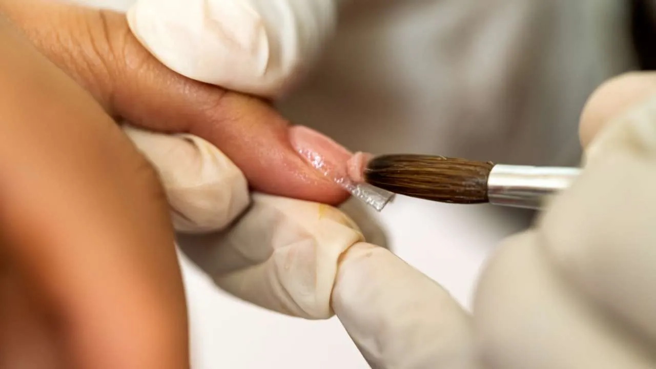 Nail technician using an e-file near a client’s nail.