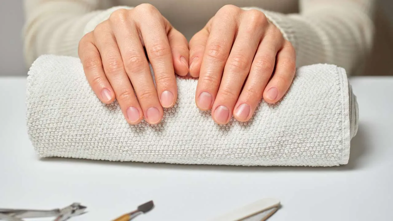 Hands with a pale pink manicure resting on a towel.