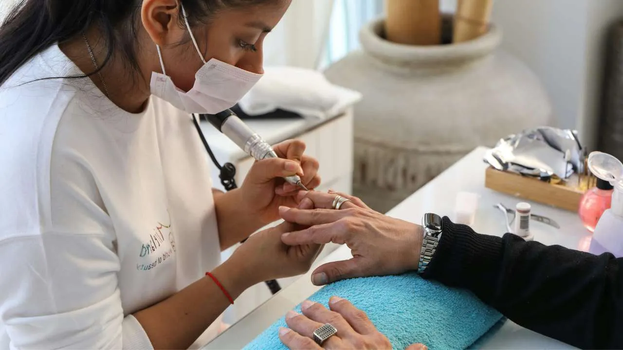 Nail technician using an e-file during a manicure.